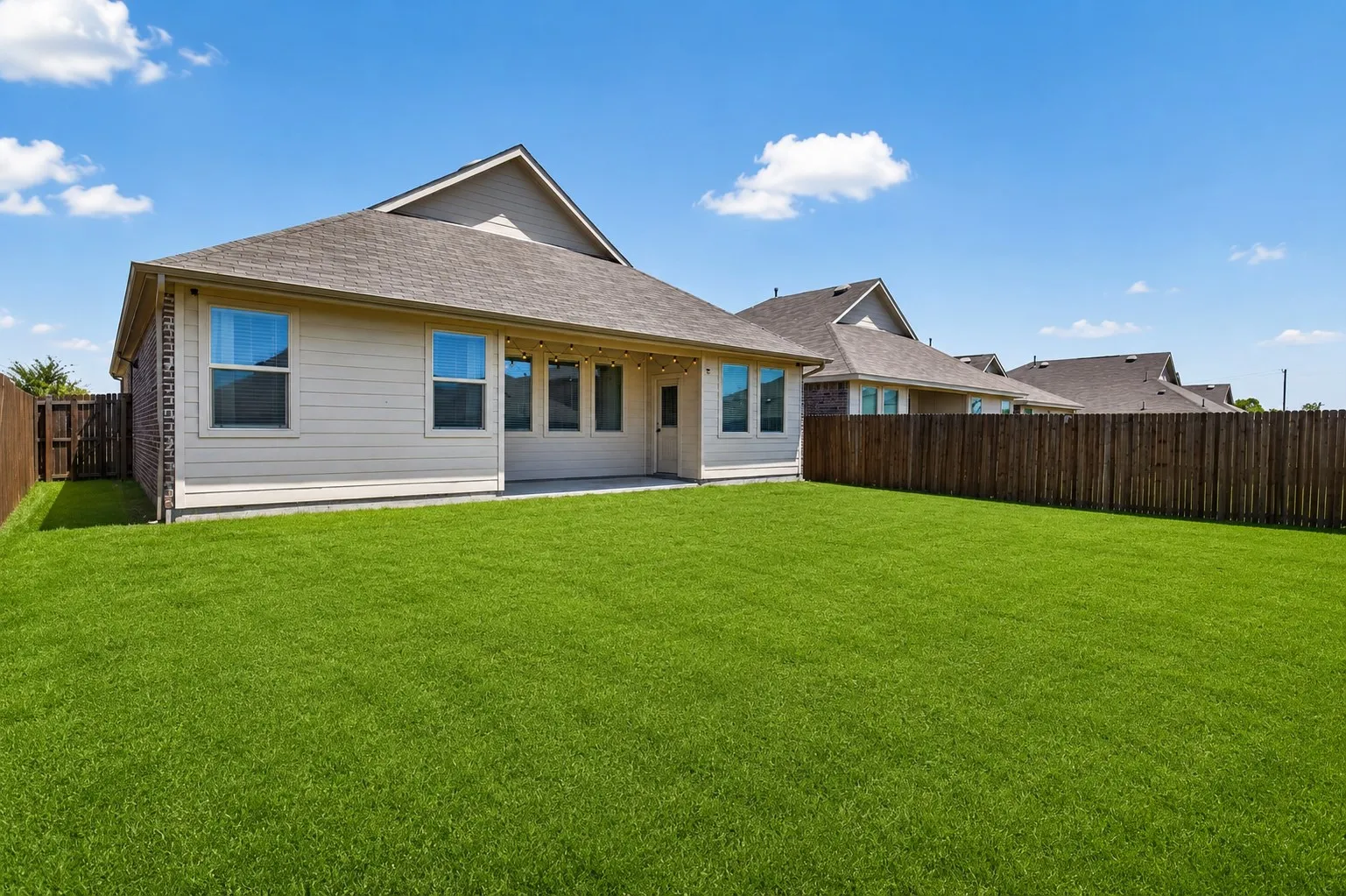 Spacious backyard featuring a manicured lawn, full privacy fencing, and a concrete patio