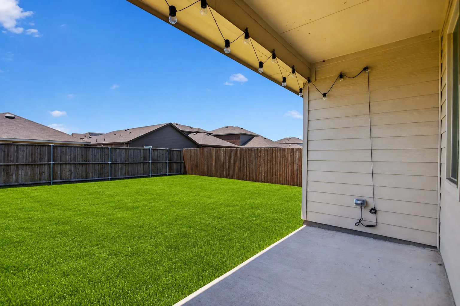 Expansive backyard with a manicured lawn, wood fencing, and a concrete patio