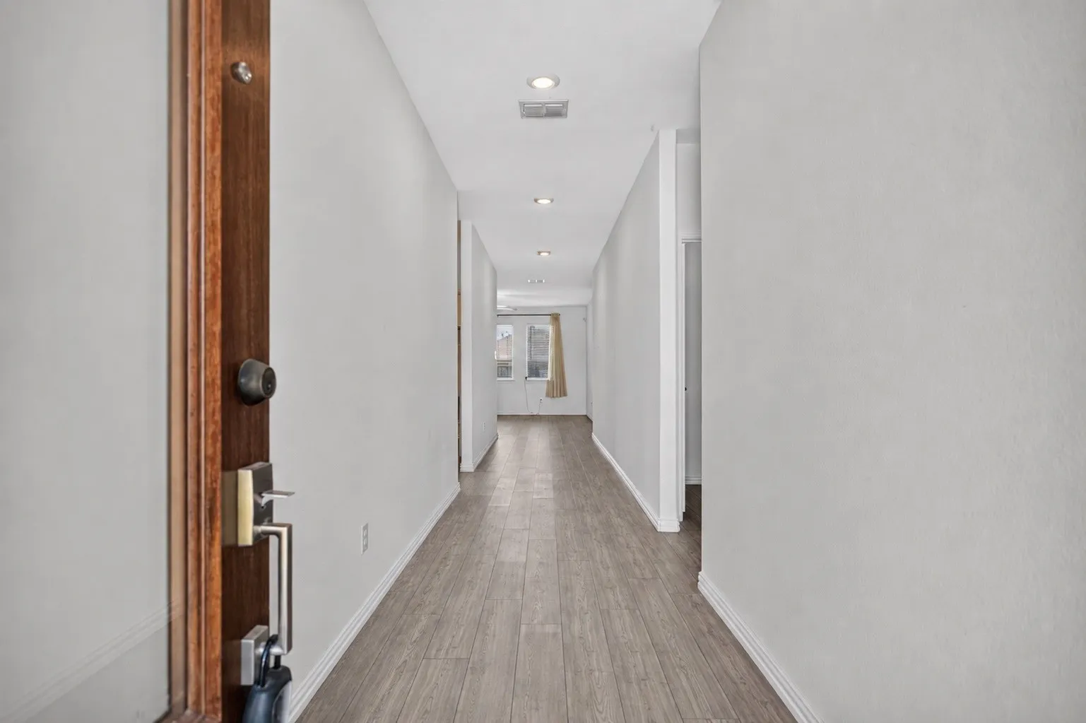Wood-finish flooring extending through a hallway with recessed lighting and neutral wall tones