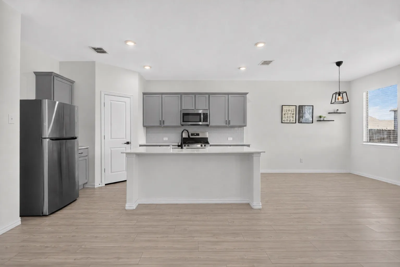 Wood-finish flooring, recessed lighting, island with integrated sink, stainless steel appliances, and grey cabinetry