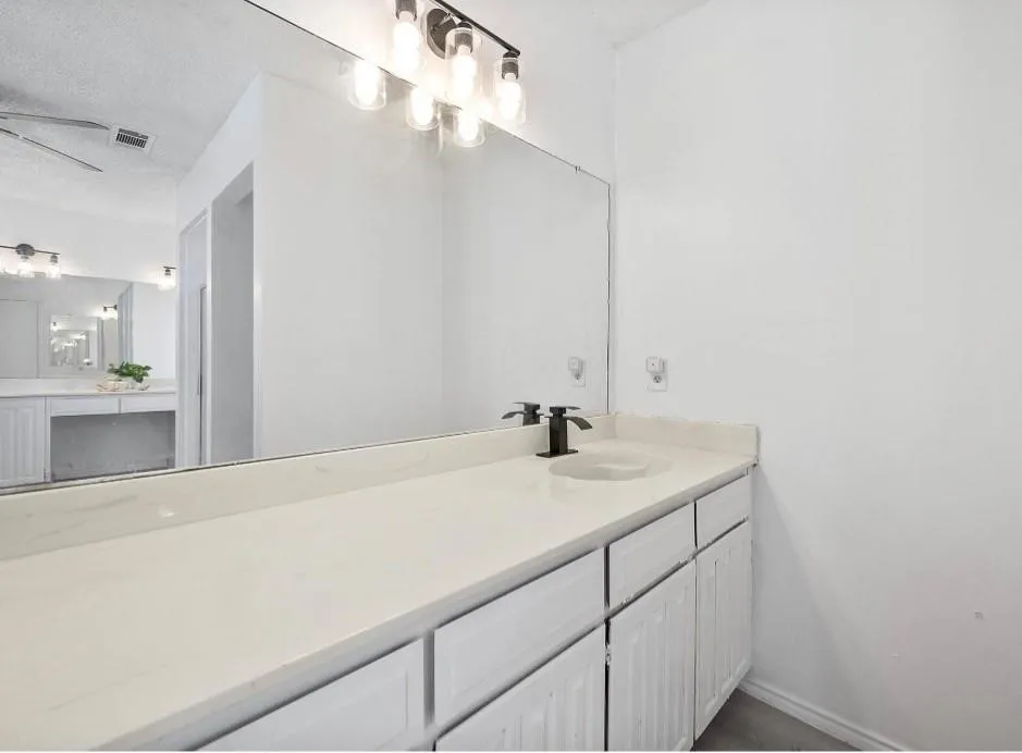 Extended vanity with dual sinks, white cabinetry, integrated lighting, and dark-finished fixtures