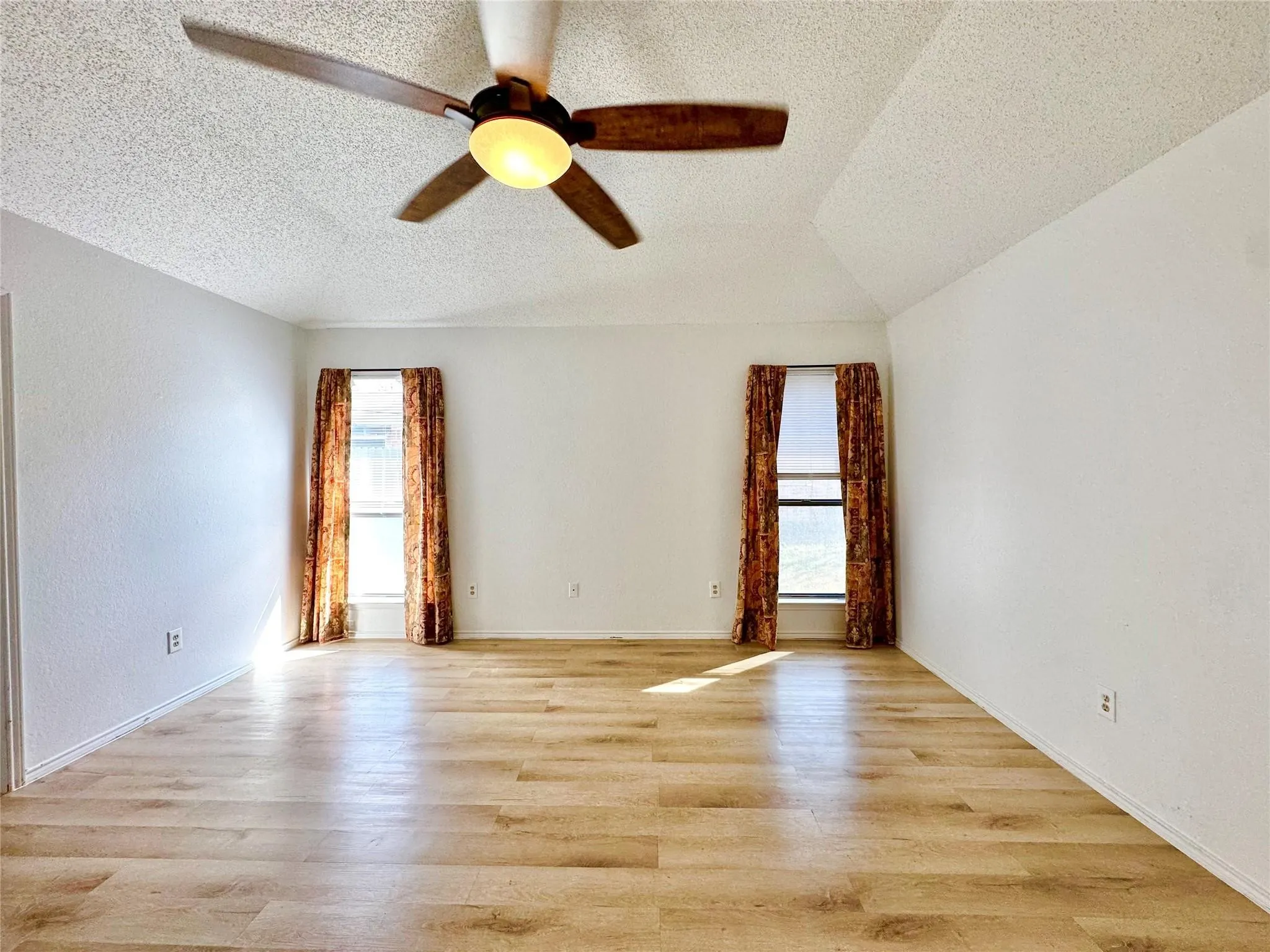 Vaulted ceiling with a ceiling fan, wood-finish flooring, and two windows