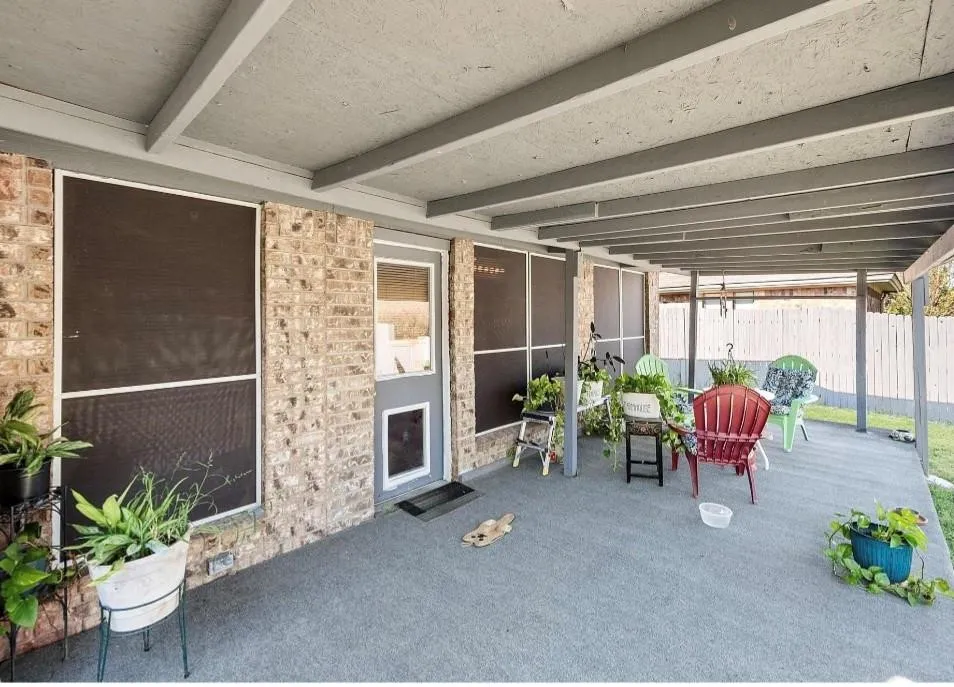 Covered patio featuring a concrete floor, exposed beam ceiling, brick exterior wall, and screened windows