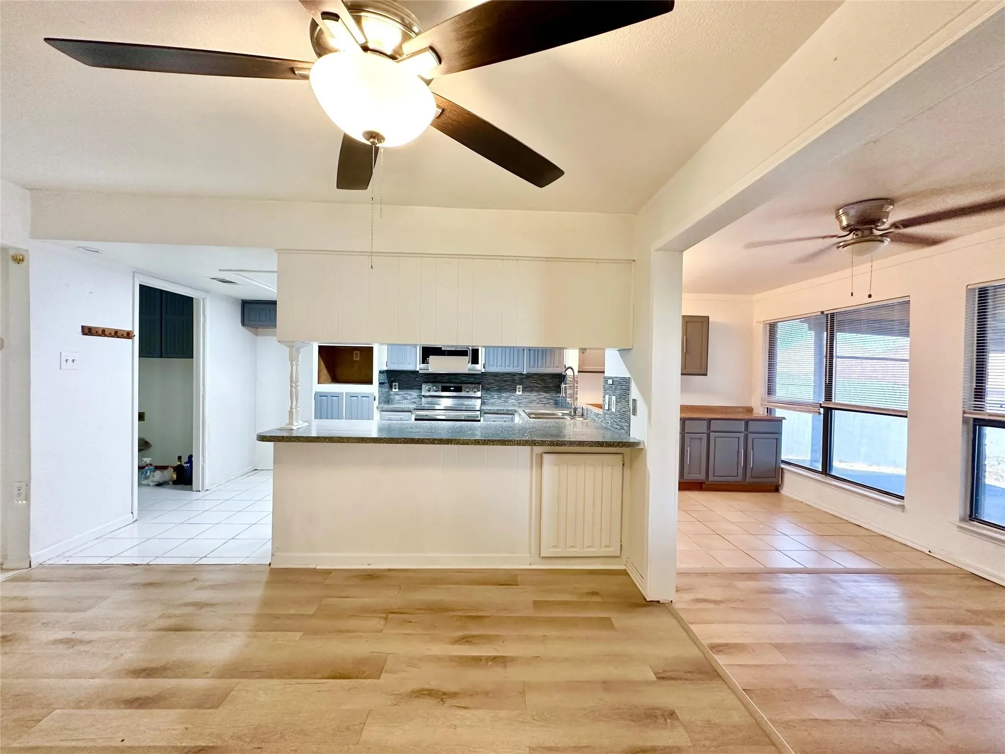 Wood-finish flooring, ceiling fan, kitchen with light-colored cabinetry, stone-finish countertops, and stainless steel appliances
