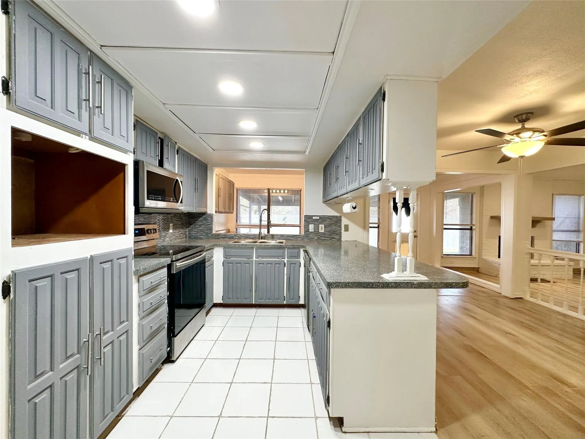 Kitchen featuring white tile flooring, gray cabinetry, stainless steel appliances, and a gray speckled countertop
