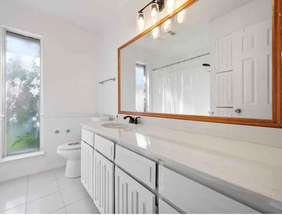 White tile flooring, double vanity with white cabinetry, integrated sink, and an expansive mirrored wall