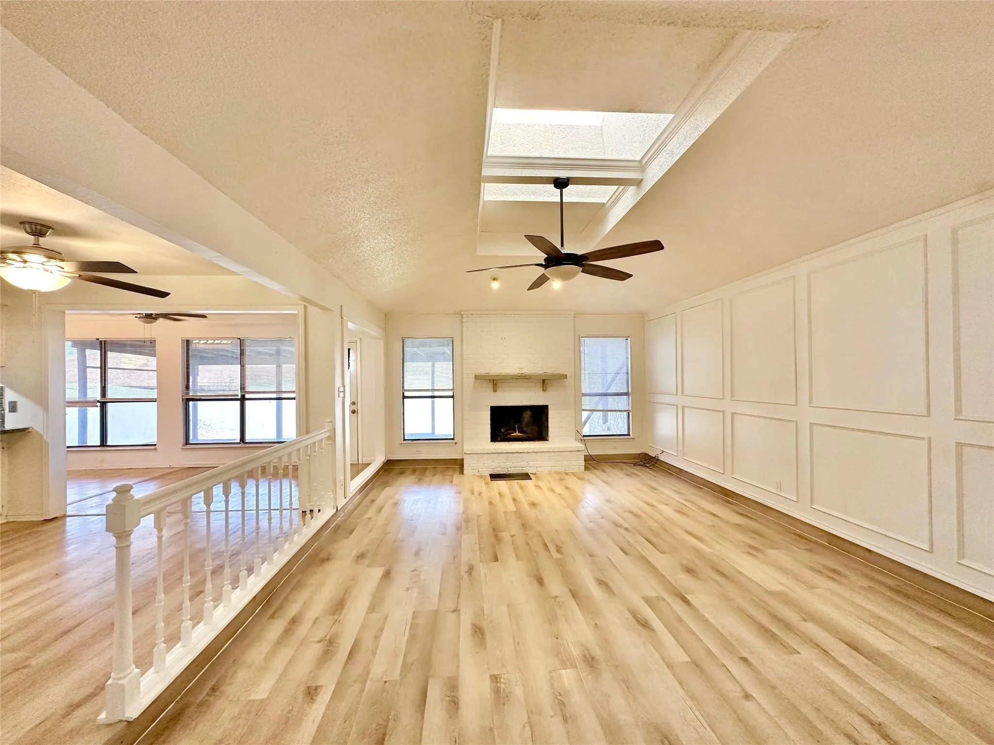 Vaulted ceiling, skylight, wood-finish flooring, white paneled accent wall, and a fireplace with a mantel