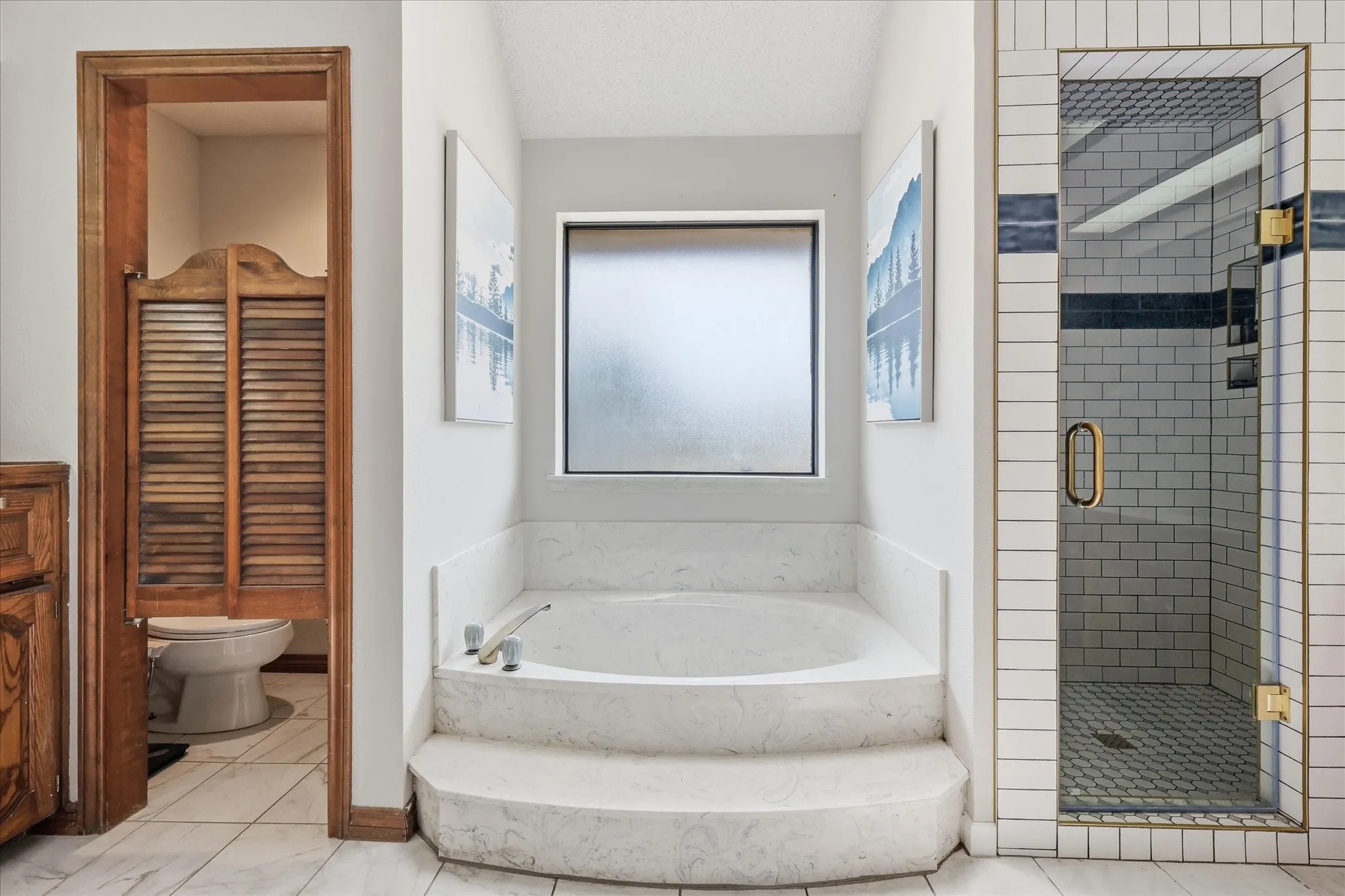 Built-in soaking tub with tiered steps, frosted window, and adjacent glass-enclosed shower with subway tile