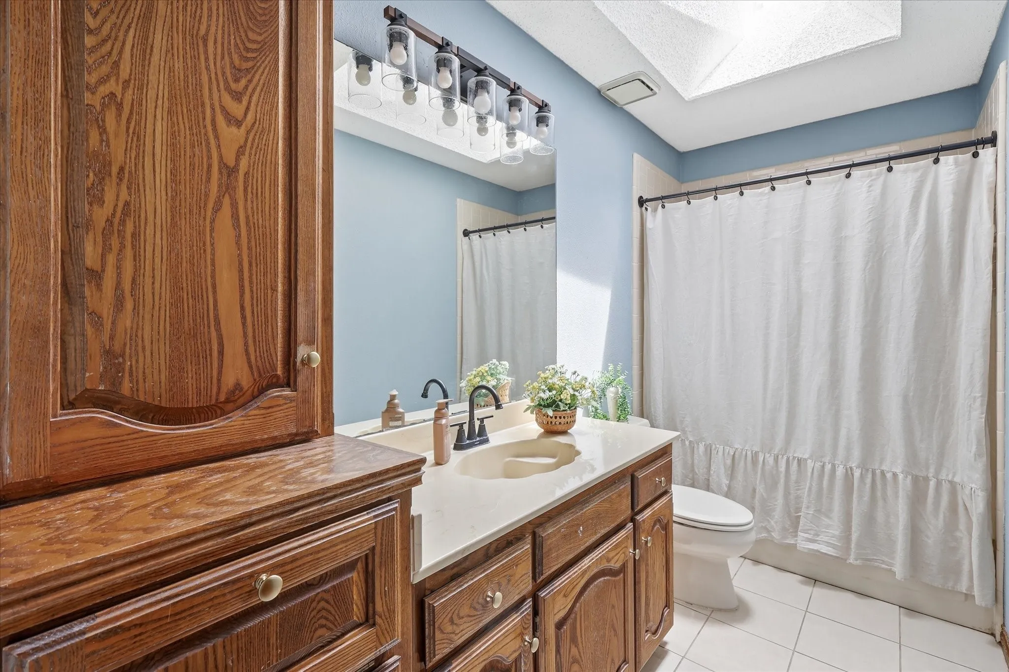 Bathroom featuring wood cabinetry, white tile flooring, a skylight, a vanity with an integrated sink, and an overhead light fixture