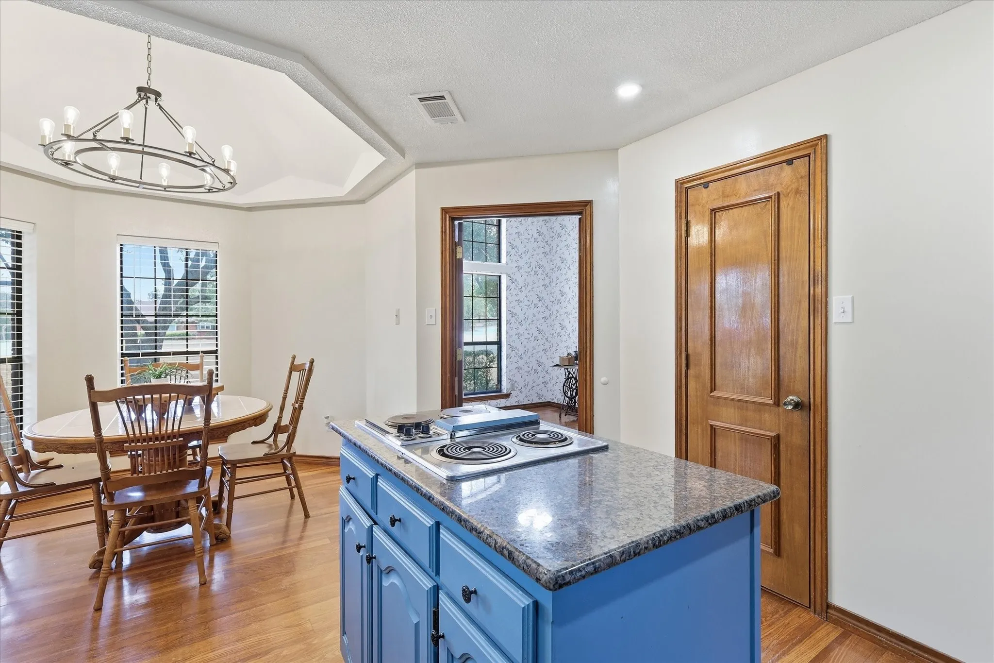 Kitchen island with a built-in electric cooktop, granite countertop, and light blue cabinetry