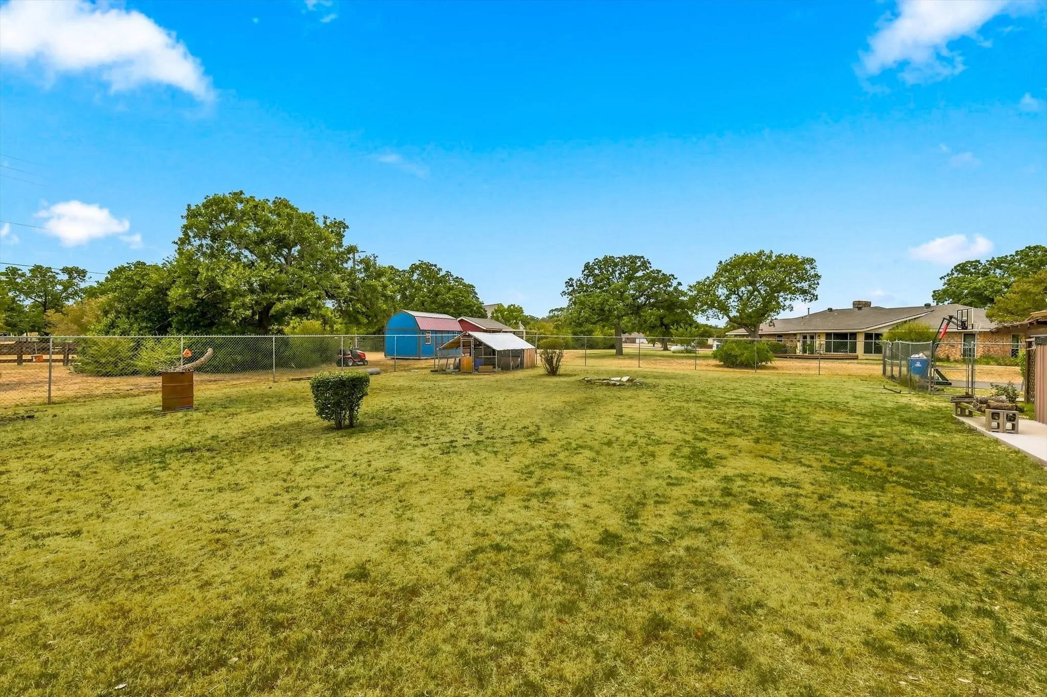 Expansive grass lawn with mature trees and a chain-link fence