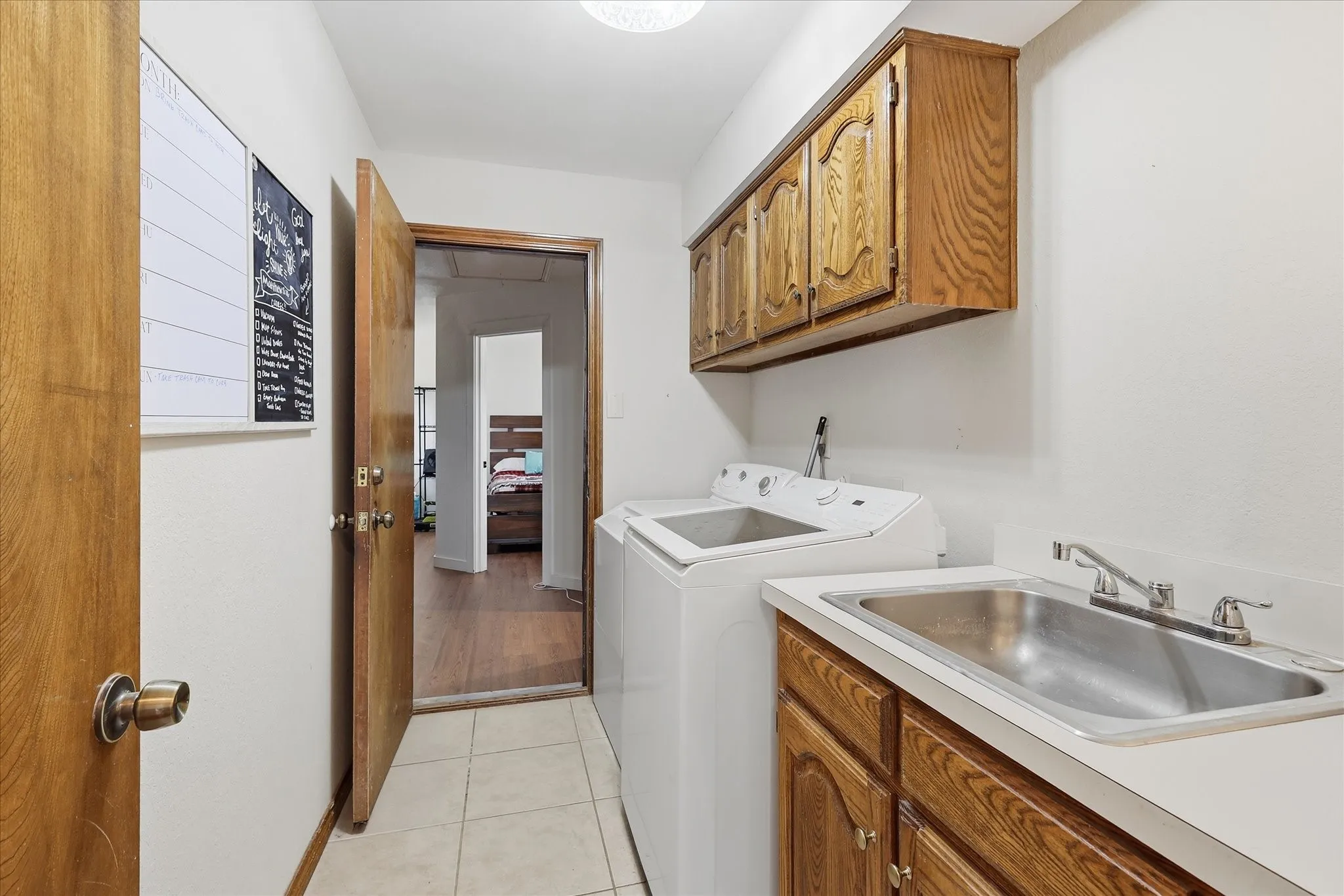Laundry area featuring wood-finish cabinetry, a utility sink with a countertop, and neutral-toned floor tiling