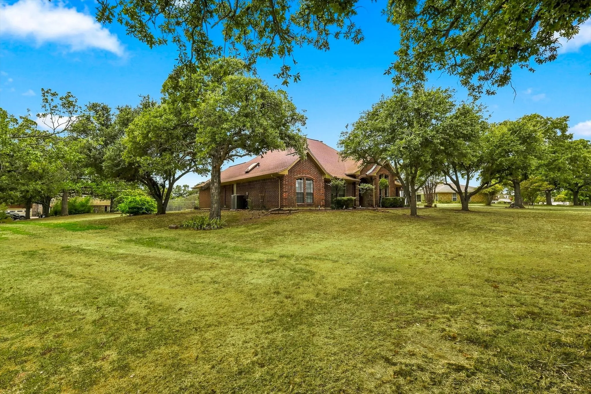 Expansive lawn with mature trees, brick exterior, and a red shingle roof