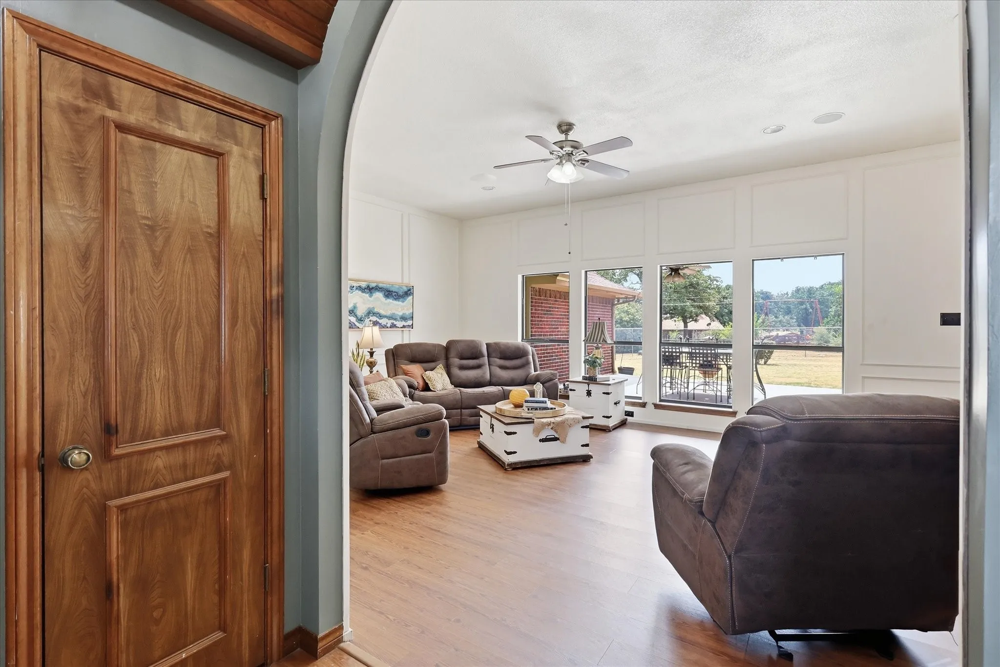 Archway entry to a room featuring wood-finish flooring, a ceiling fan with integrated lighting, and multiple large windows