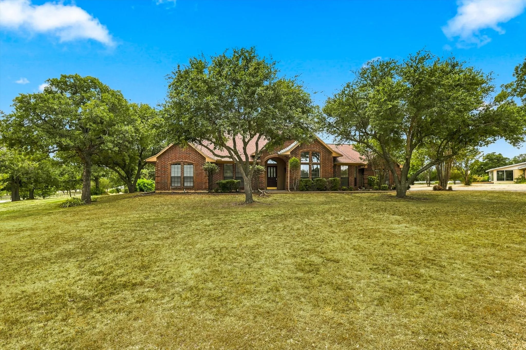 Expansive front lawn with mature trees and a brick exterior residence featuring a gabled roof