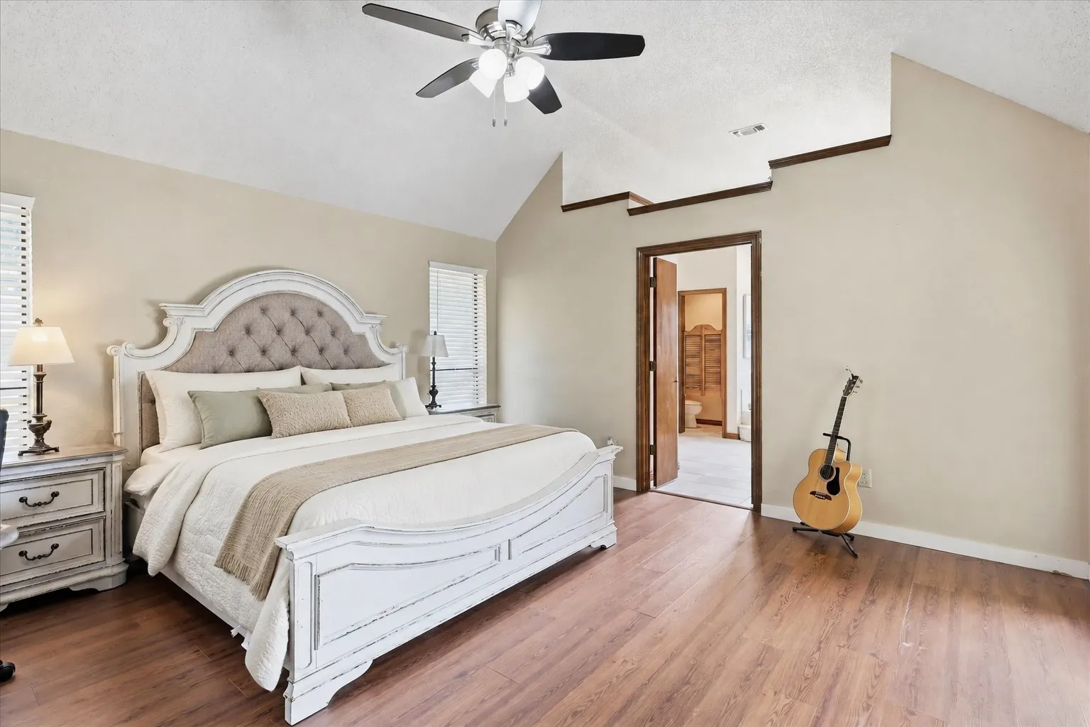 Vaulted ceiling with exposed wood beams, ceiling fan with integrated lighting, wood-finish flooring, and a doorway opening to an additional room