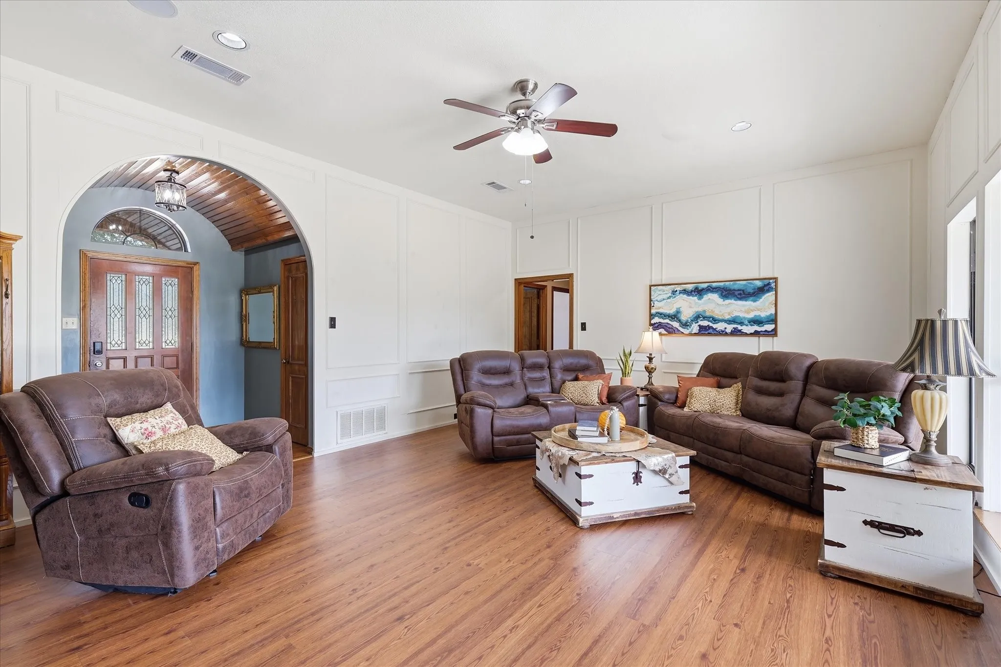 Wood-finish flooring throughout, bright white walls with panel molding, and an arched entryway featuring a wood-panel ceiling