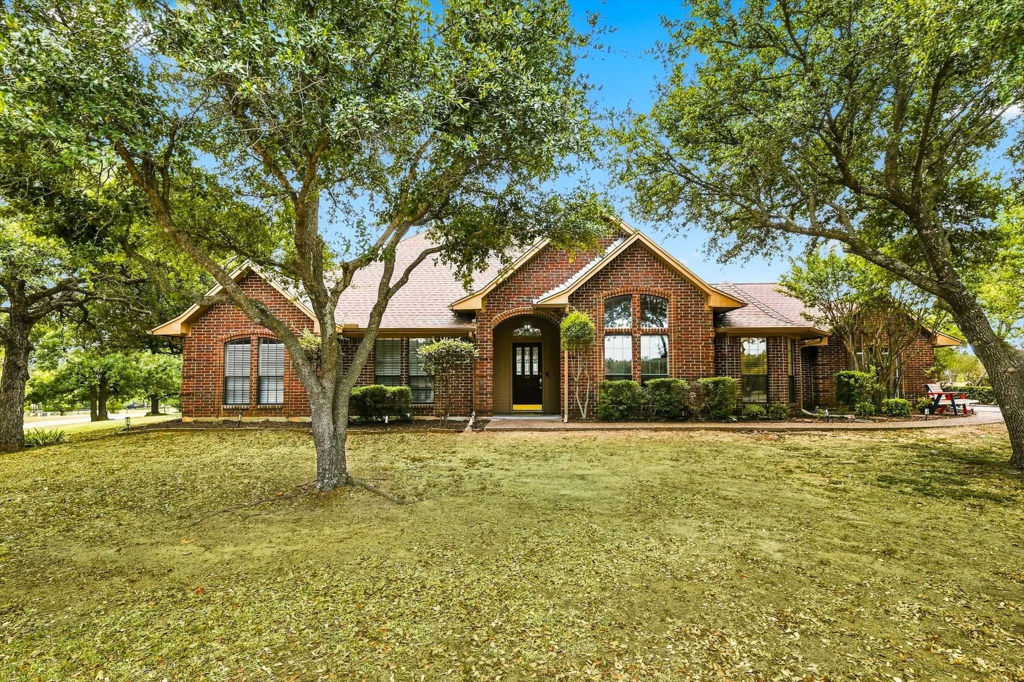 Brick exterior with gabled roof lines, arched entry, mature trees, and landscaped foundation plantings