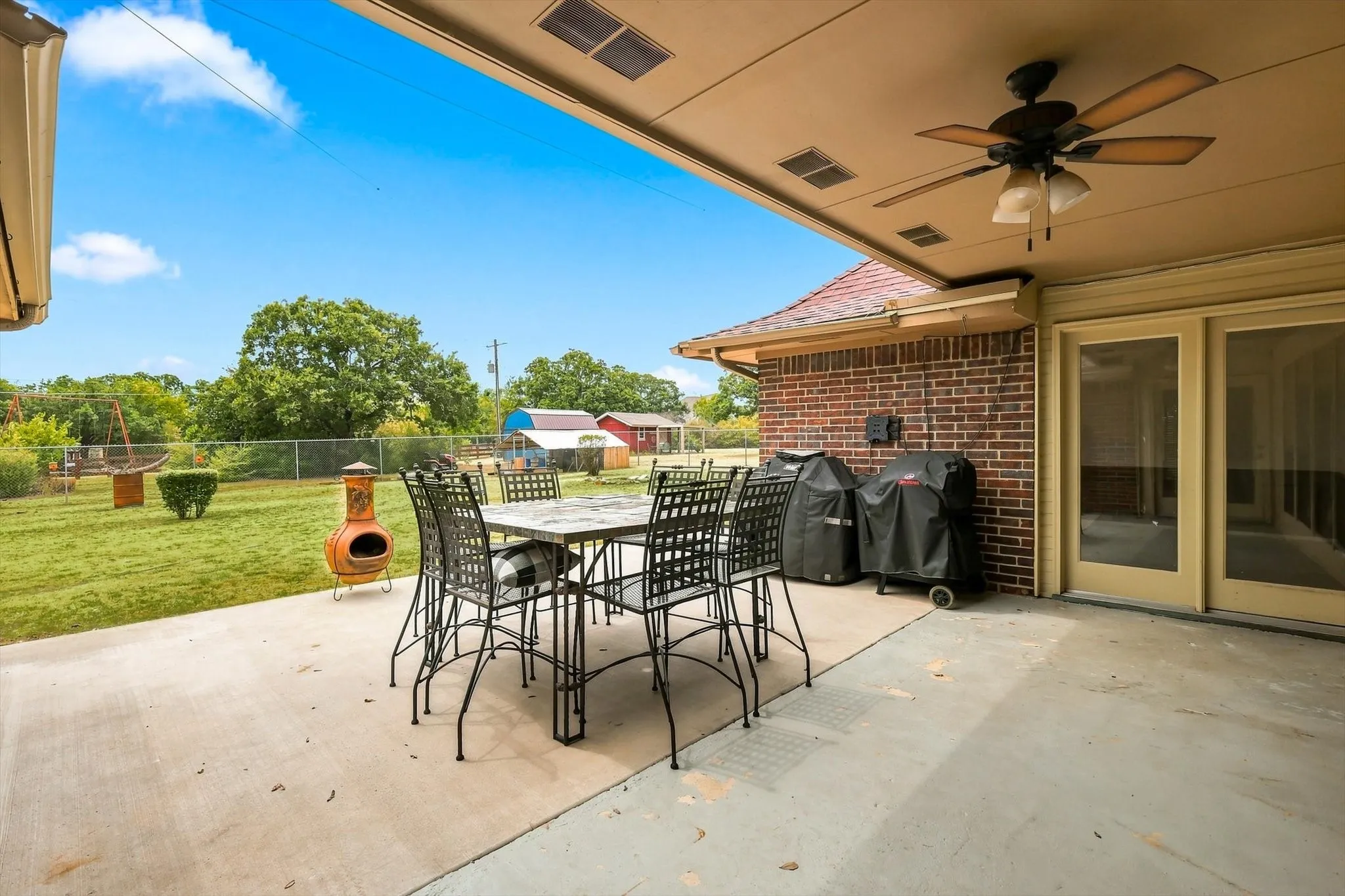 Covered concrete patio with ceiling fan, brick exterior, and dual glass sliding doors