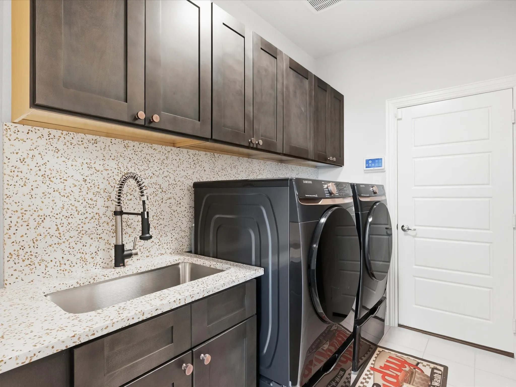 Built-in upper and lower cabinetry, speckled solid surface countertop, stainless steel utility sink, and a modern gooseneck faucet