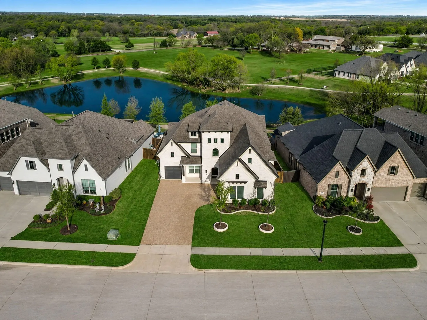Expansive property featuring a large pond, lush green landscaping, a paved driveway, and a two-story home with a multi-gabled roof