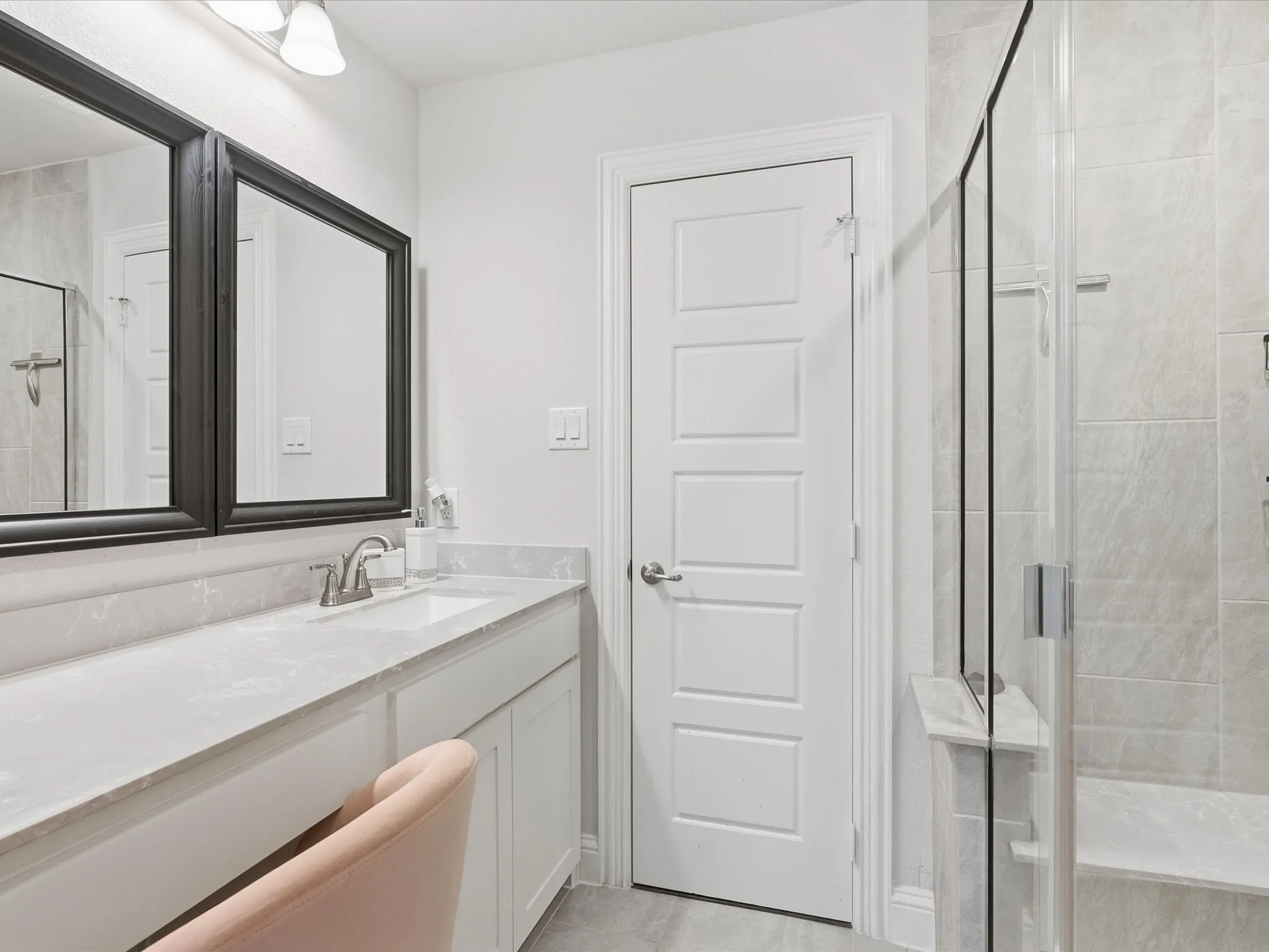 Dual framed mirrors, vanity with integrated sink, glass-enclosed shower, tiled shower walls, and a built-in shower bench