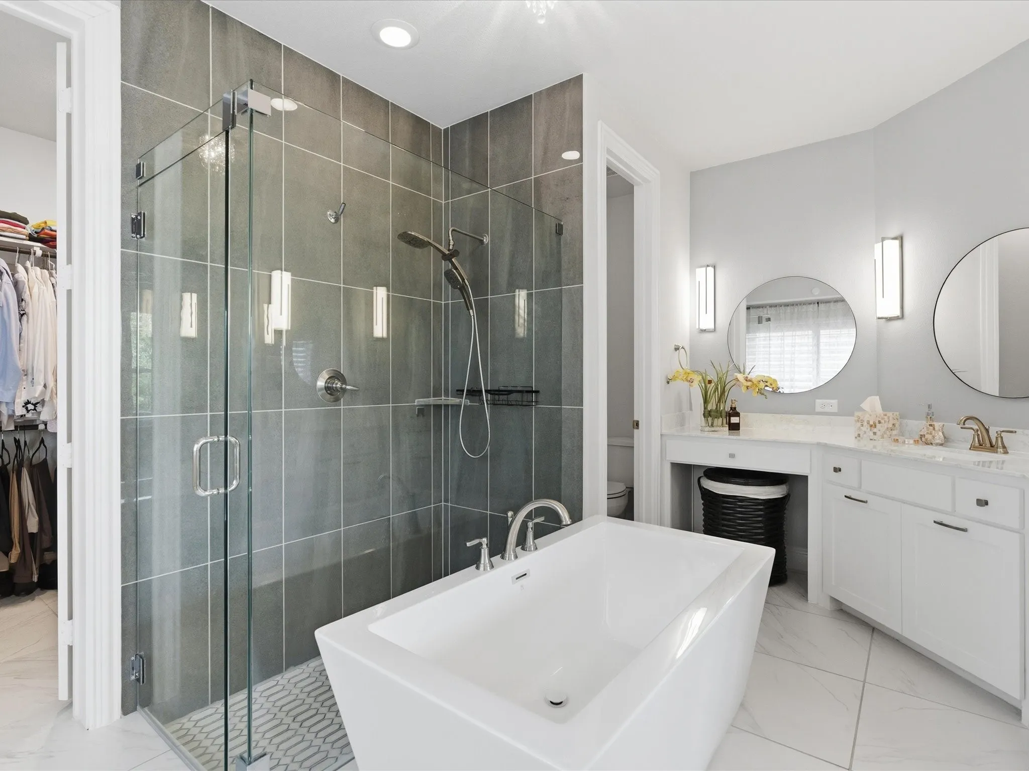 Freestanding soaking tub, frameless glass shower enclosure with tile surround, dual vanity with undermount sinks, and two circular mirrors