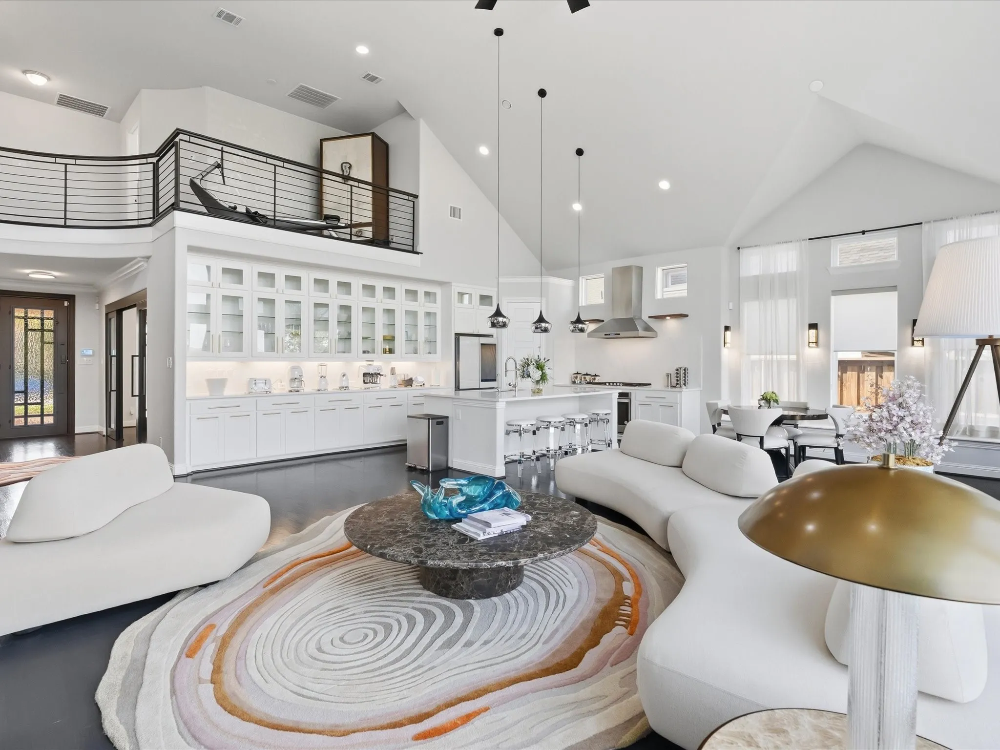 Vaulted ceilings, a second-story interior balcony with metal railing, an extensive built-in display cabinet with glass doors, a kitchen island with seating, and dark wood-finish flooring