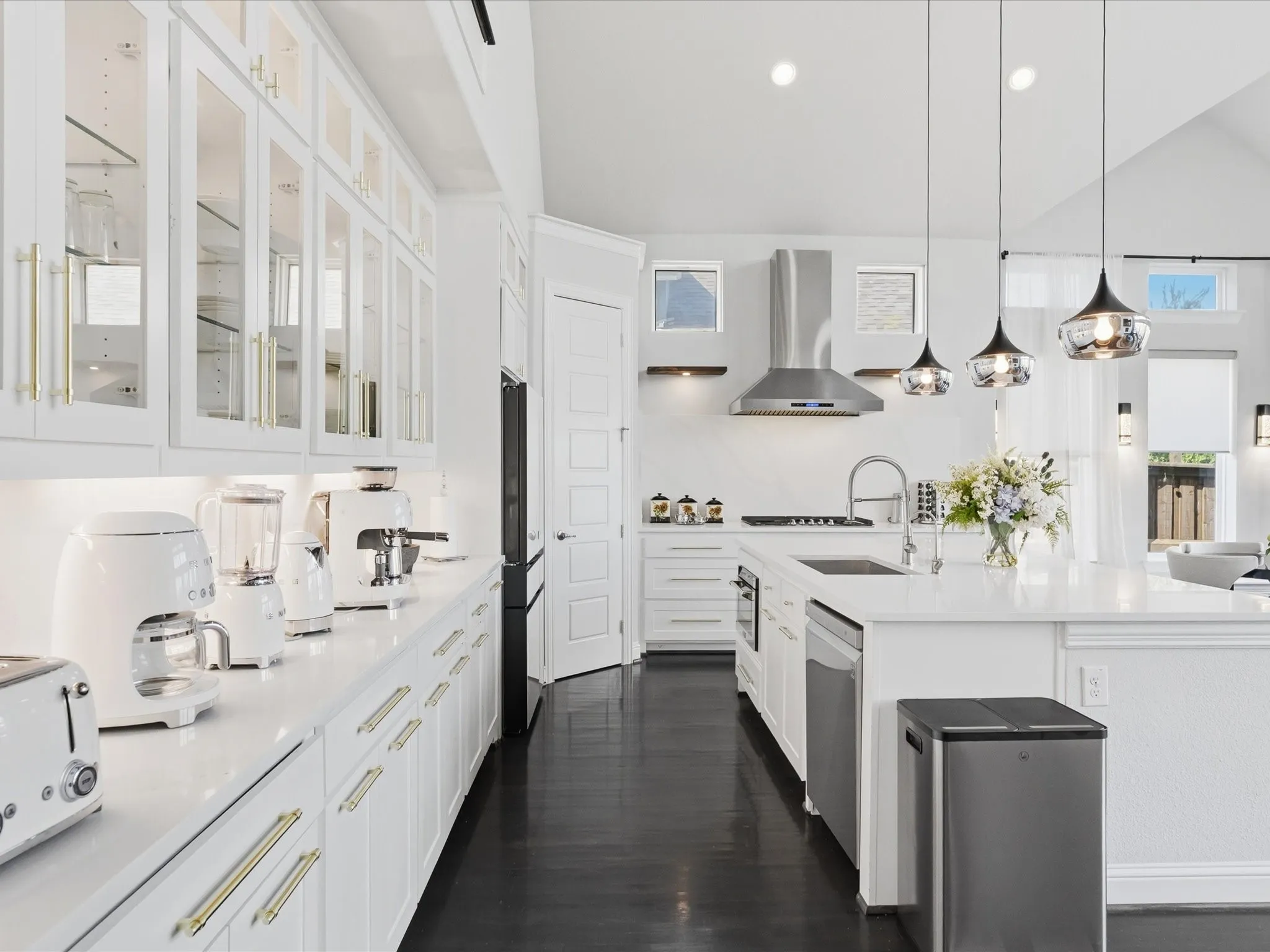 Open-concept kitchen with crisp white cabinetry, gold-finish hardware, stainless steel appliances, and a central island with an integrated sink