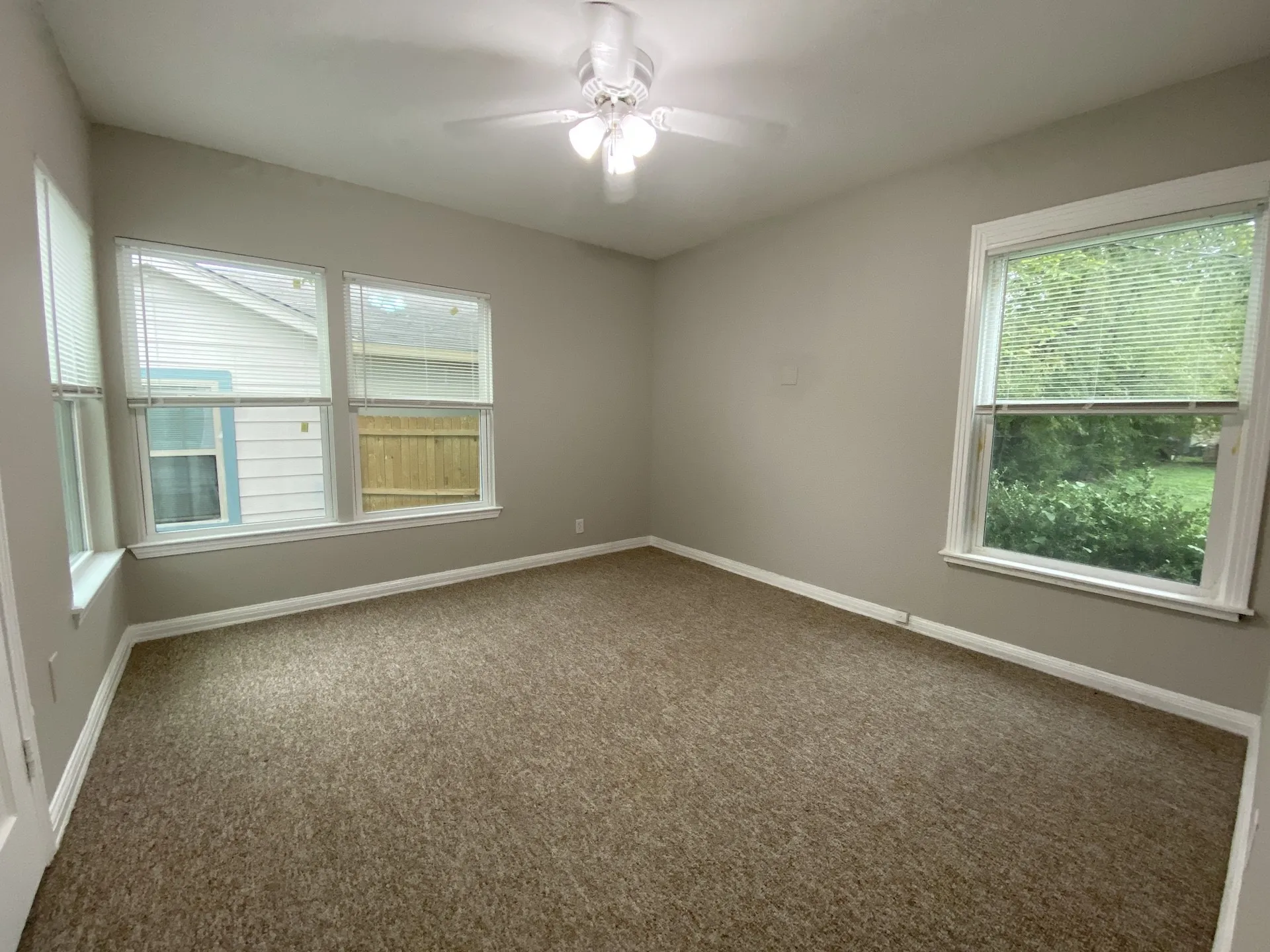 Bedroom with a ceiling fan, multiple windows with blinds, and neutral-toned carpet