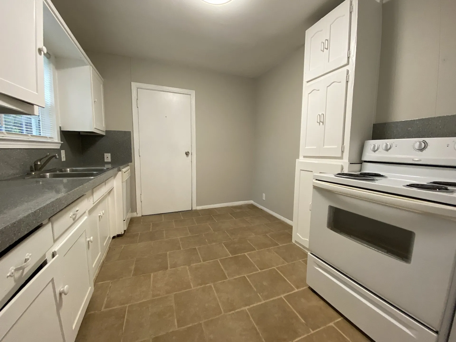 Kitchen featuring white cabinetry, gray countertops, a stainless steel double basin sink, and tile flooring