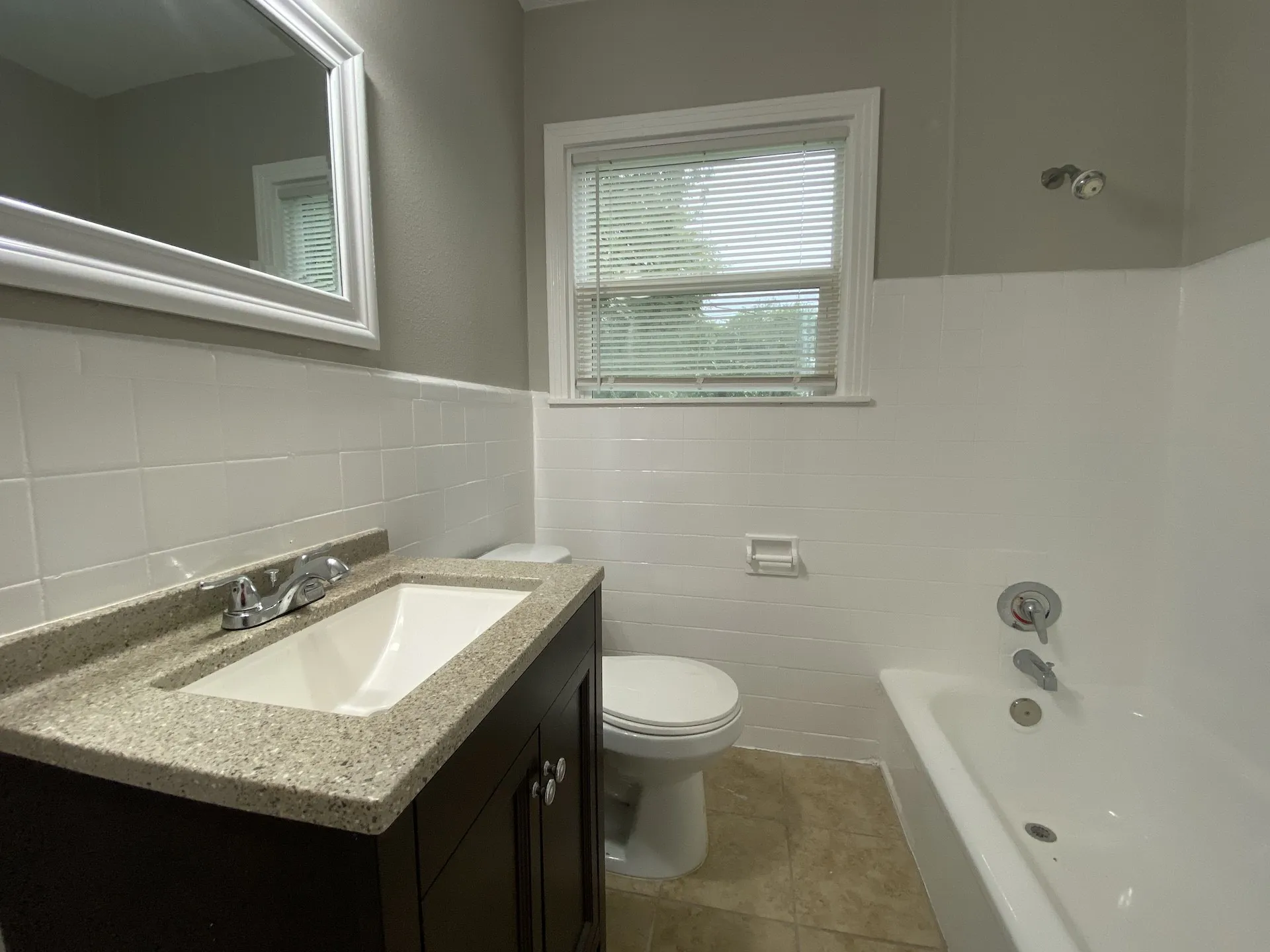 Bathroom featuring a vanity with an integrated sink and light-colored countertop, white wall tiling, a white bathtub, and a window with blinds