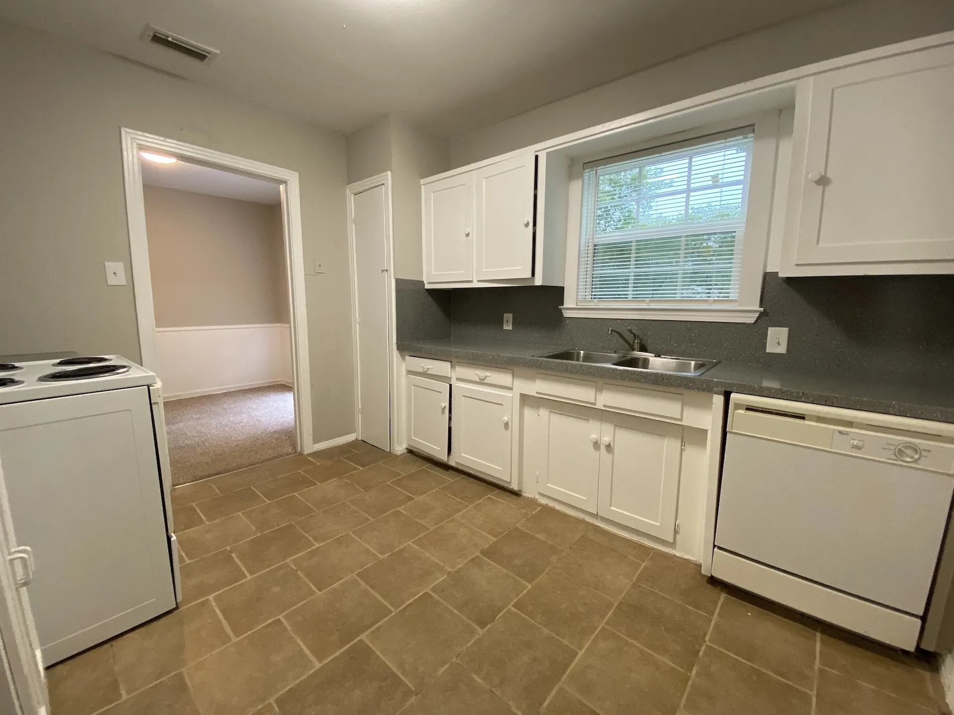 White cabinetry with dark countertops, double basin stainless steel sink, and ceramic tile flooring