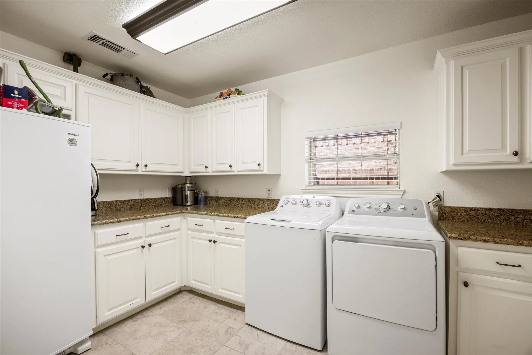 Dedicated laundry room featuring white cabinetry with granite-style countertops, stainless steel appliances, recessed ceiling lighting, and neutral tile flooring