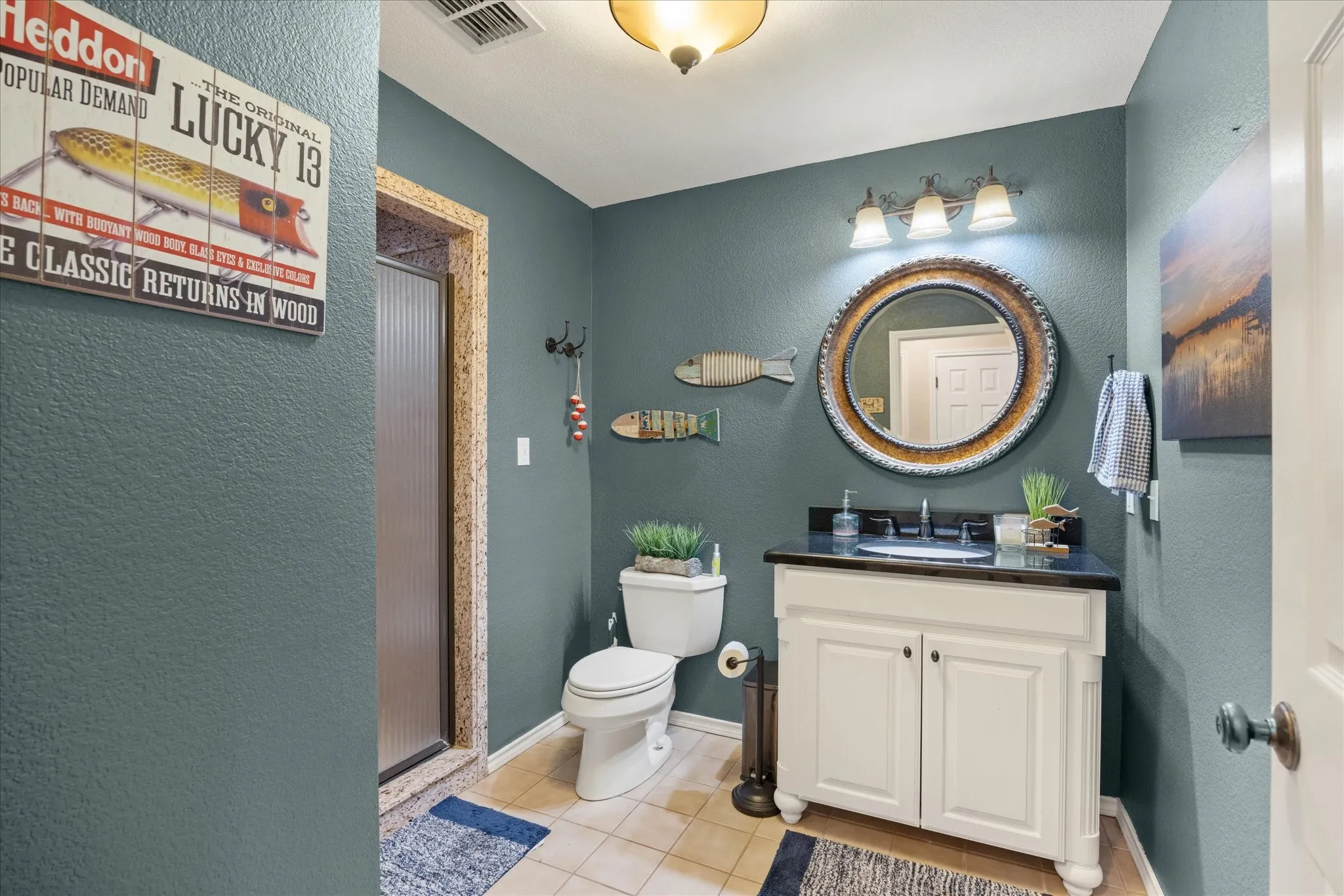 White vanity with dark countertop, circular mirror, and three-light fixture