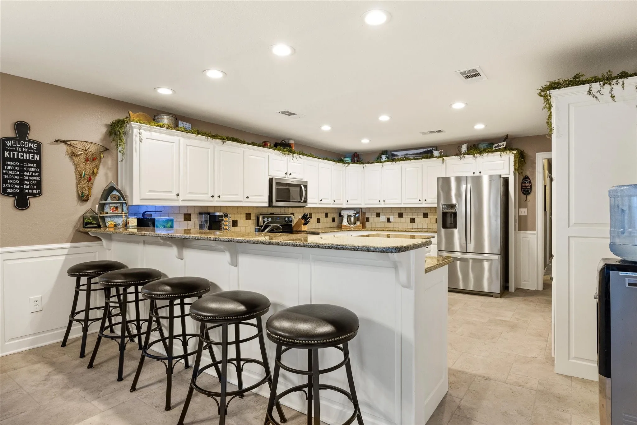 Gourmet kitchen featuring white cabinetry, stainless steel appliances, granite countertops, and a large island with seating for three
