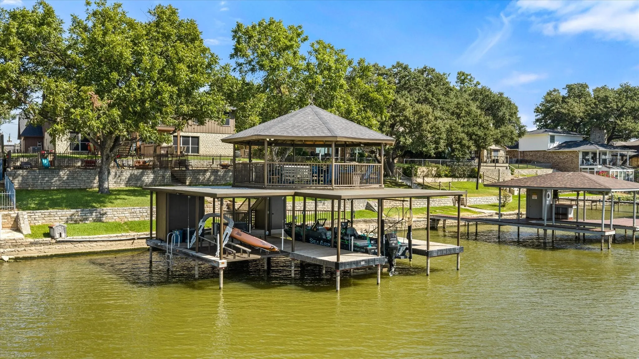 Waterfront property featuring a dual-level boat dock with covered upper pavilion, composite decking, and aluminum railings