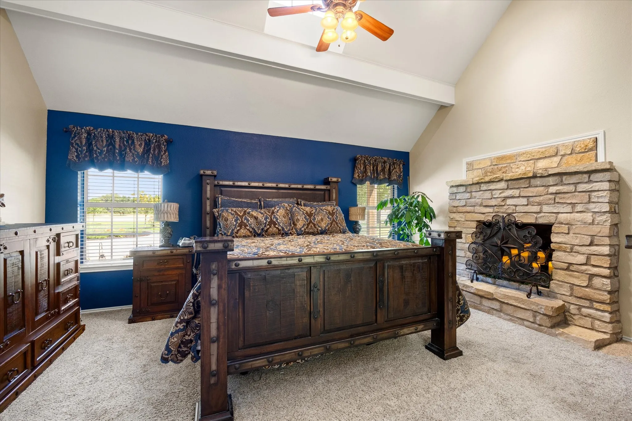Primary Bedroom with Dark Wood Bed Frame, Accent Wall in Deep Blue, Stone Fireplace, Ceiling Fan, and Carpeted Flooring