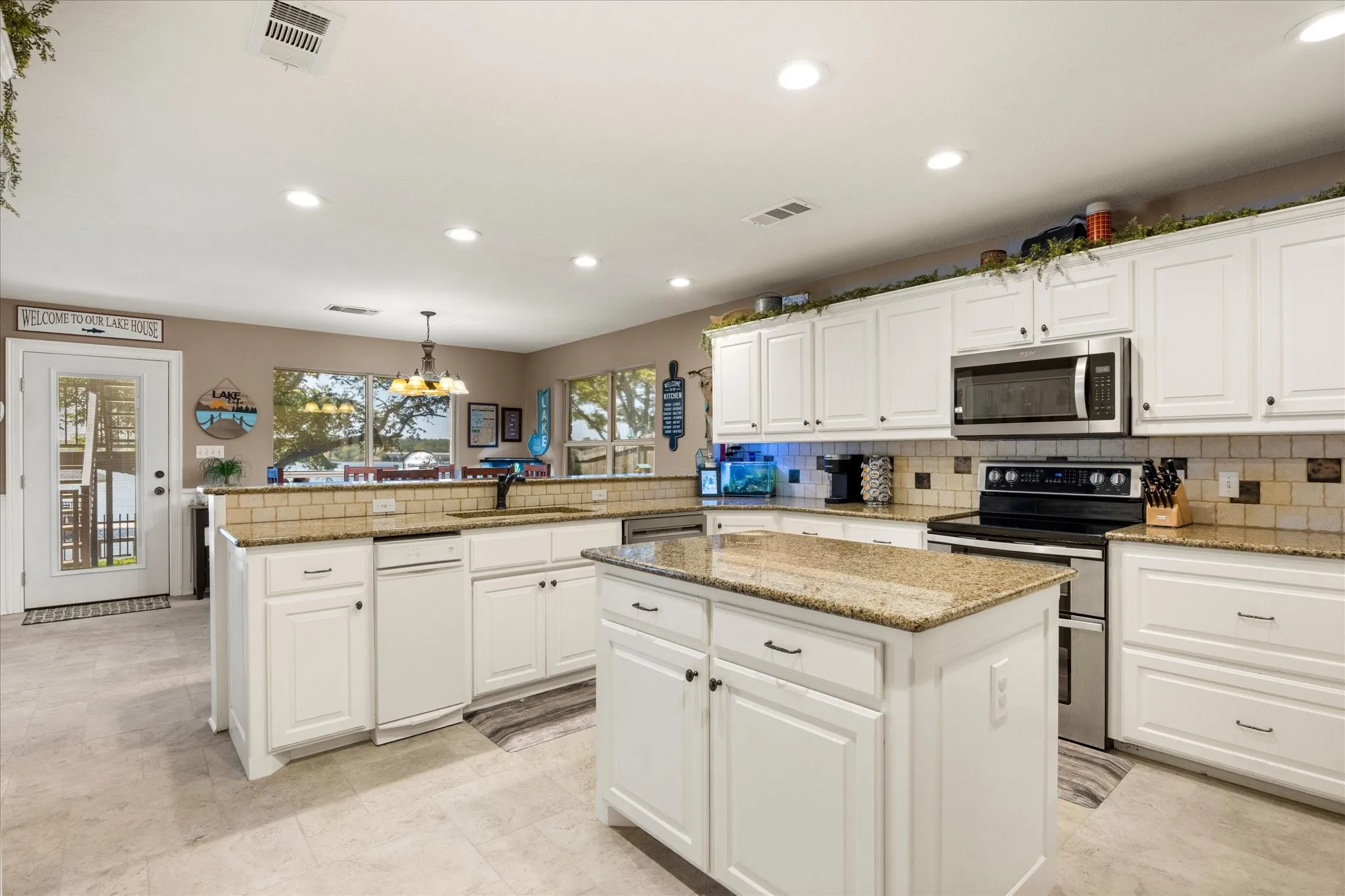 Spacious kitchen featuring white cabinetry, granite countertops, a large center island with prep space, stainless steel appliances including a gas range and built-in microwave, tile backsplash, and recessed lighting throughout