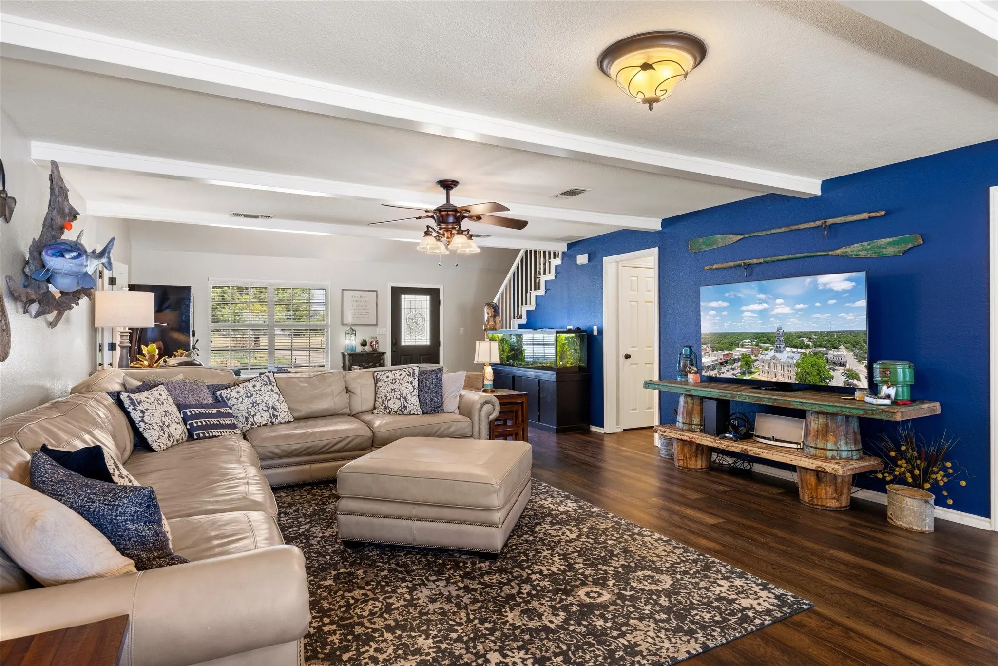 Open-concept living area featuring a curved sectional sofa arrangement, wood-finish flooring throughout, and a striking cobalt blue accent wall