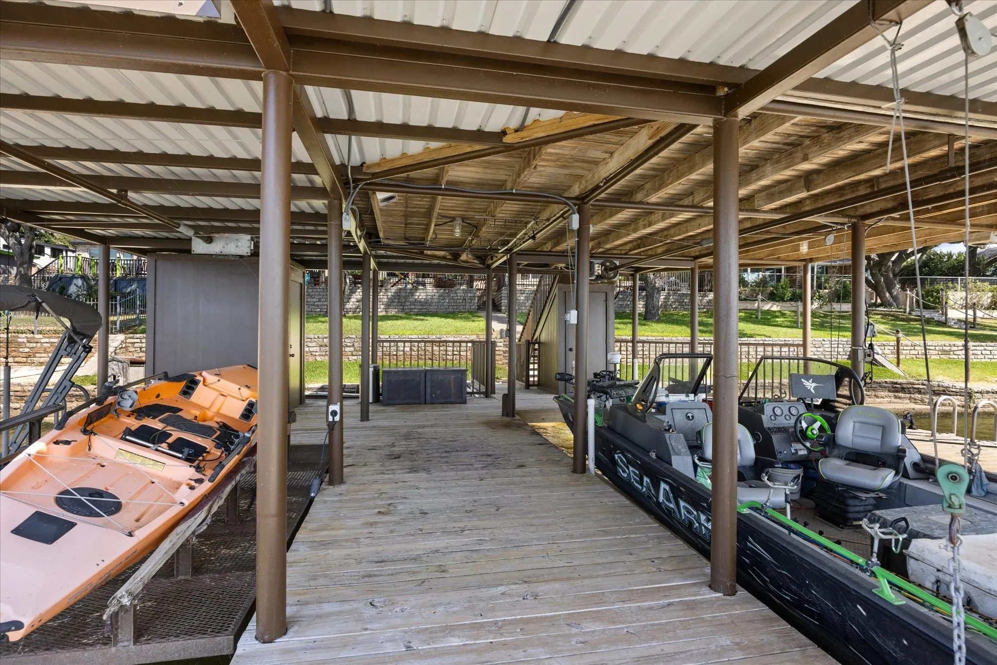 Covered boat dock featuring wood-finish decking, steel support columns, and corrugated metal roof structure