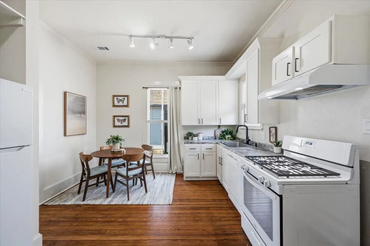 White cabinetry with black hardware, stone countertops, stainless steel sink with a black faucet, white range with an overhead vent, and wood-finish flooring