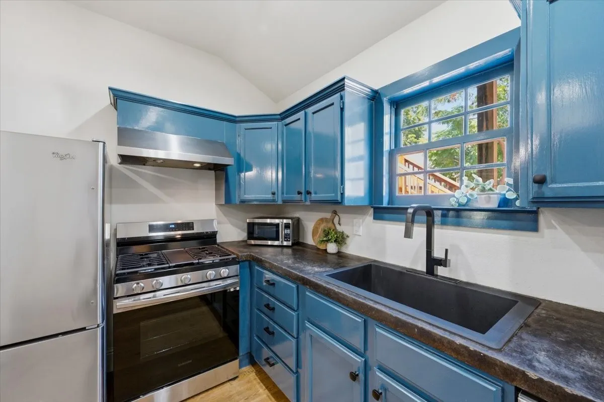 Kitchen featuring vibrant blue cabinetry, stainless steel appliances, dark countertops, and a black single-basin sink with a matte black faucet