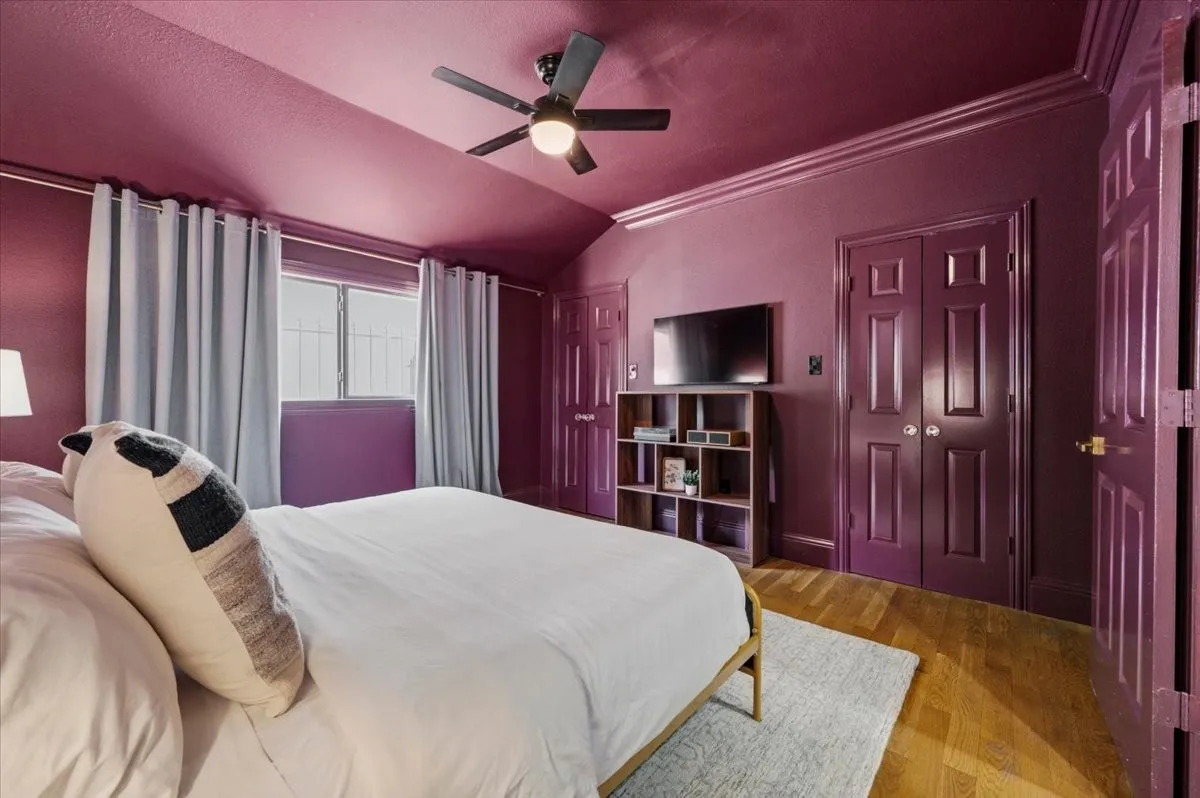 Sloped ceiling featuring a ceiling fan with integrated lighting, wood-finish flooring, two panel doors, and a window with security bars
