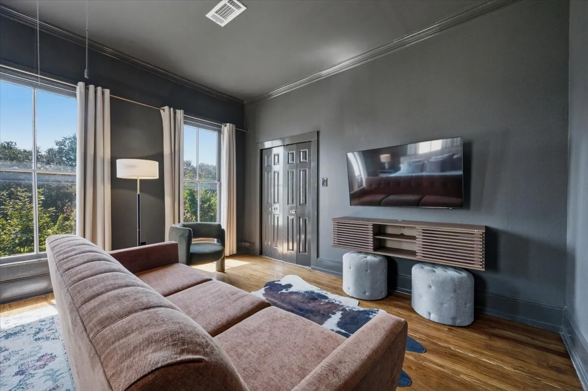 Hardwood flooring, crown molding, wall-mounted media console, and dual tall windows