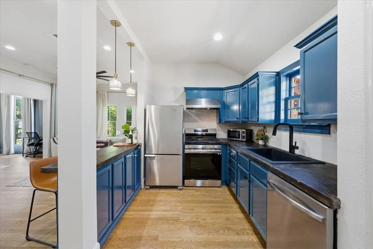 Kitchen featuring wood-finish flooring, stainless steel appliances, blue cabinetry, dark countertops, and pendant lighting