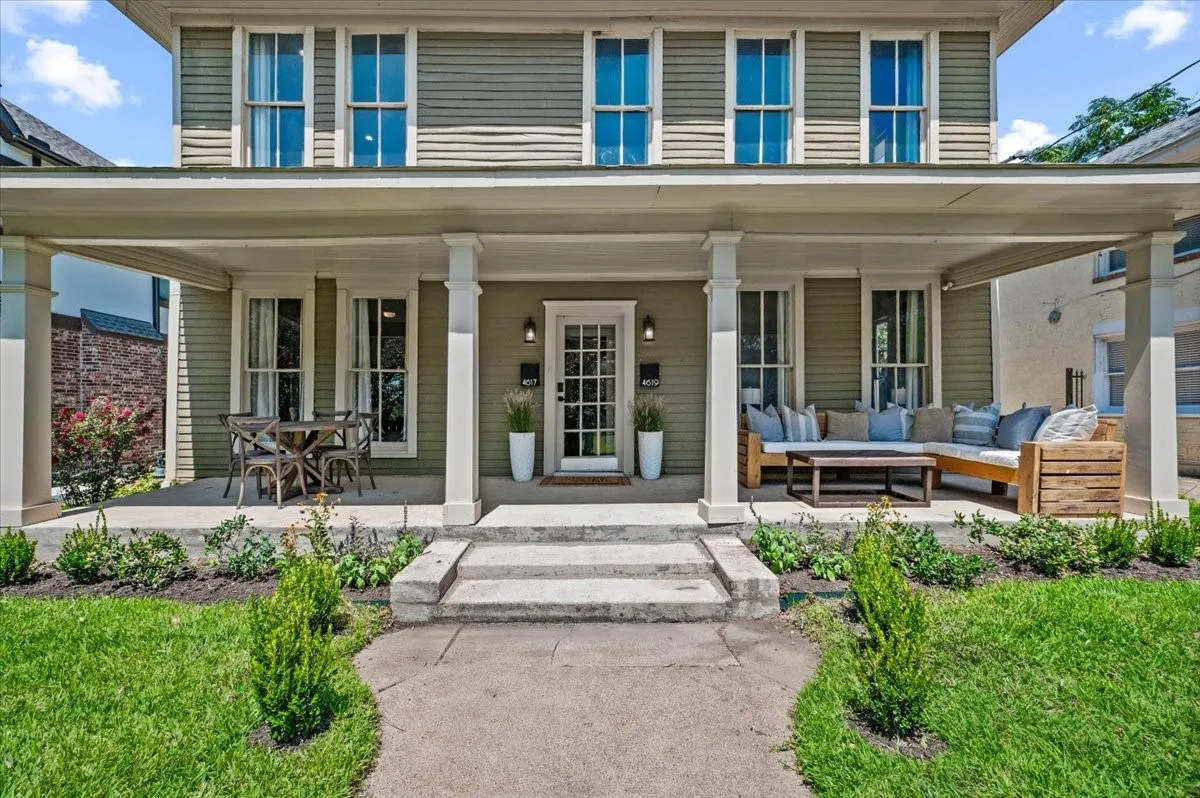 Expansive covered front porch with multiple seating areas, a classic paneled entry door, and a manicured lawn with established plantings