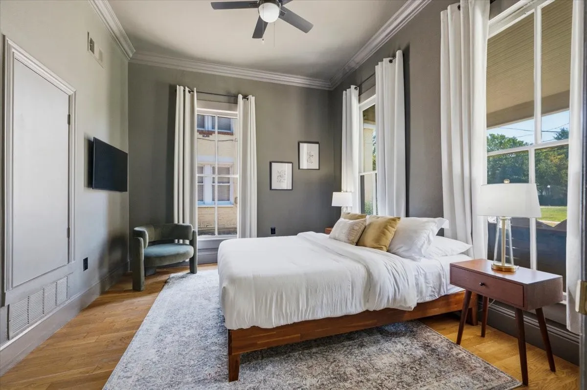 Hardwood flooring with a matte finish, ceiling fan, crown molding, and tall windows