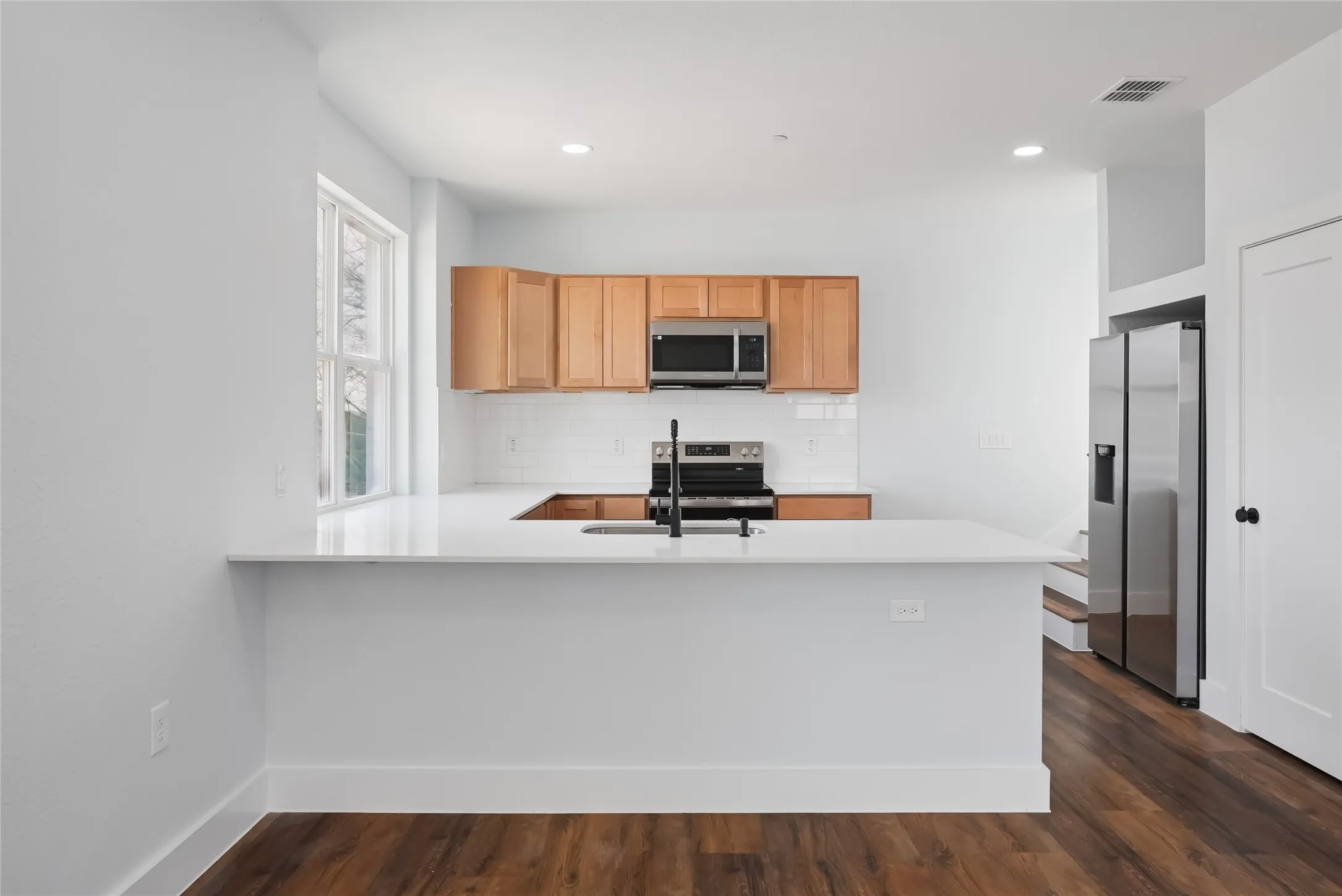Kitchen featuring wood-finish flooring, white countertops, stainless steel appliances, and light wood cabinetry with a subway tile​​‌​​​​‌​​‌‌​‌‌​​​‌‌​‌​‌​‌​​​‌​​ backsplash