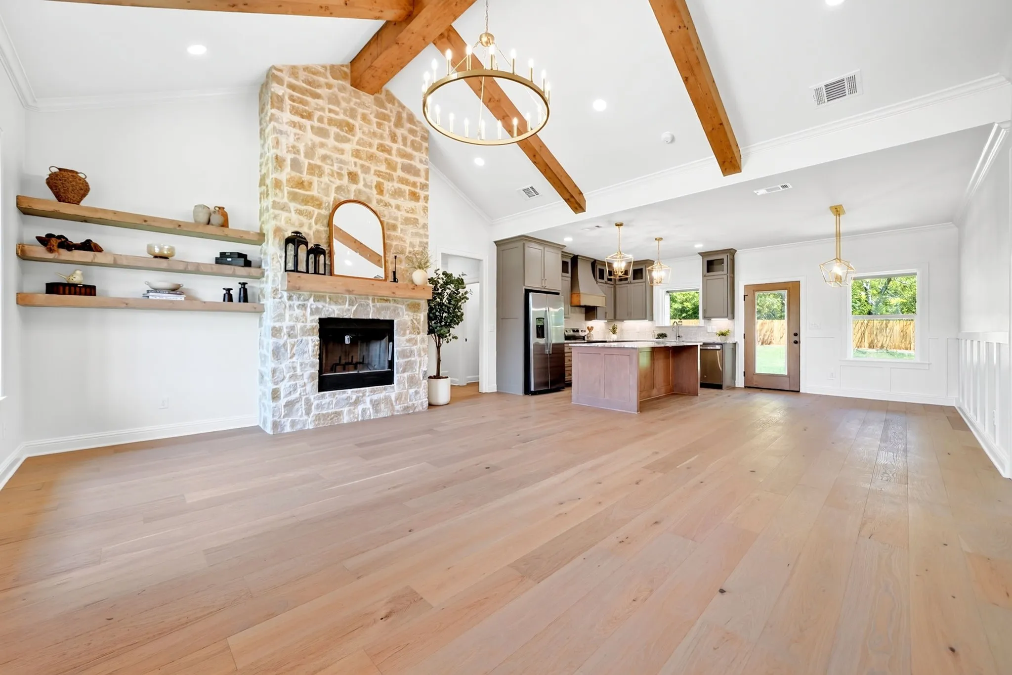 Spacious open-concept living area featuring a stone fireplace, wood-finish flooring, and vaulted ceilings with exposed wood beams